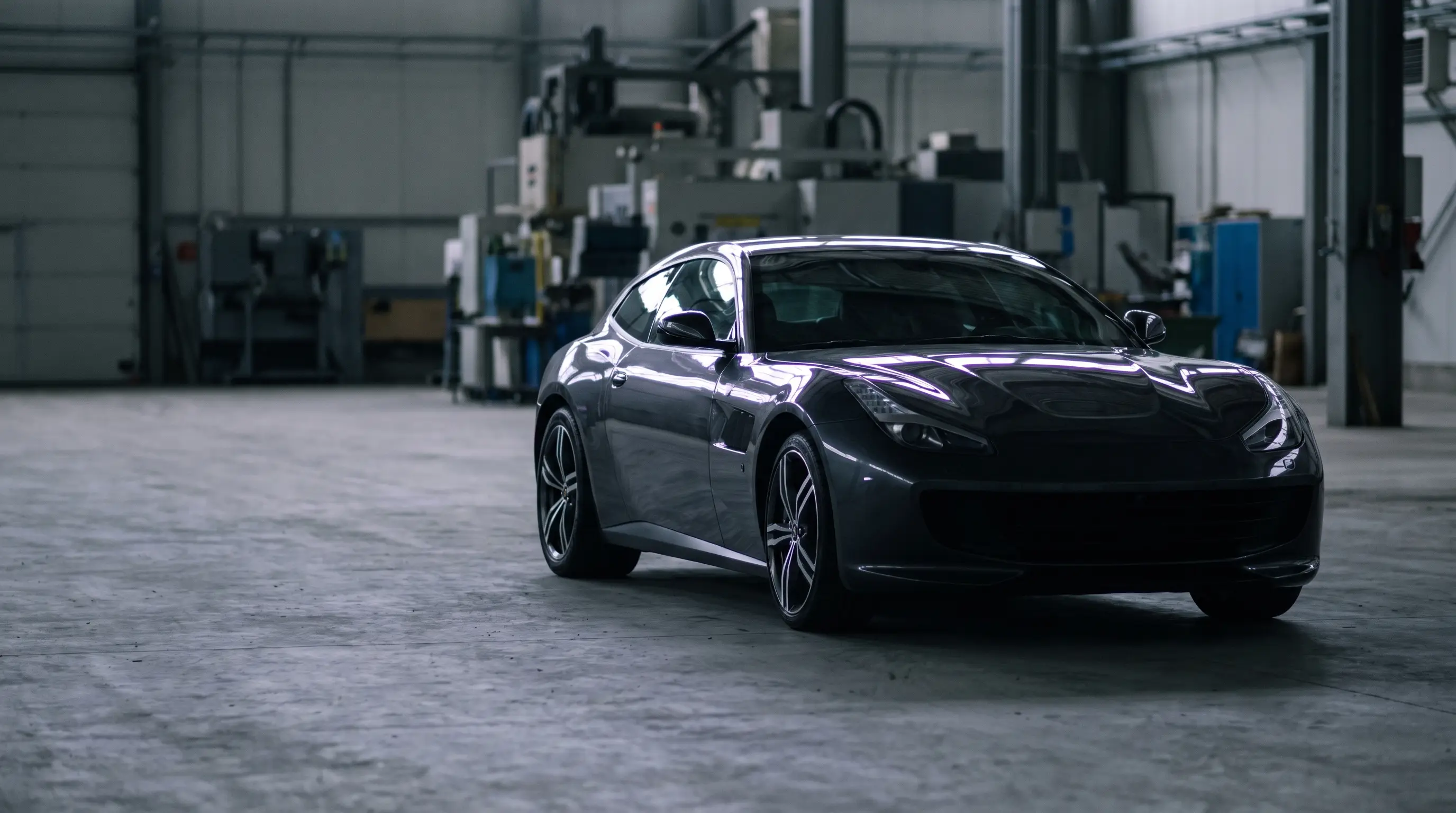 Dark grand tourer parked in a near-black garage, rim lit